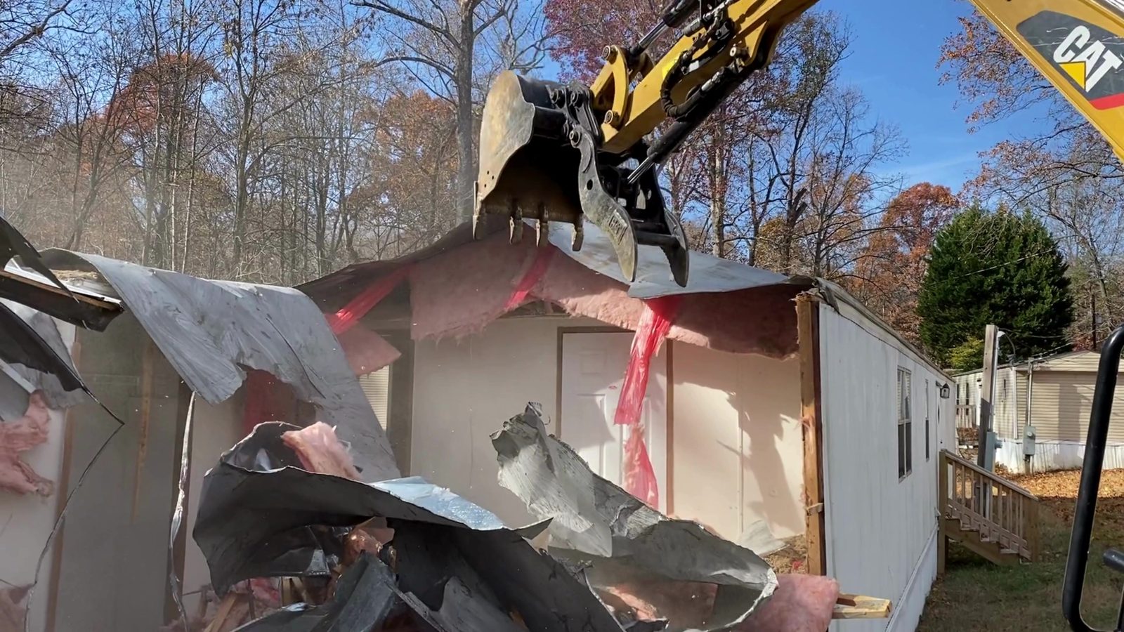 Excavator pulling siding and wall panels inward on a mobile home teardown in Denver NC