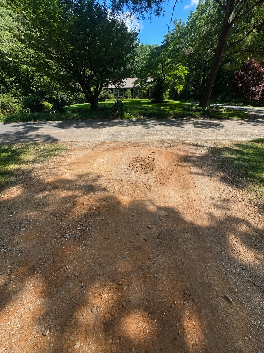 Residential gravel driveway worn down to bare red clay before repair