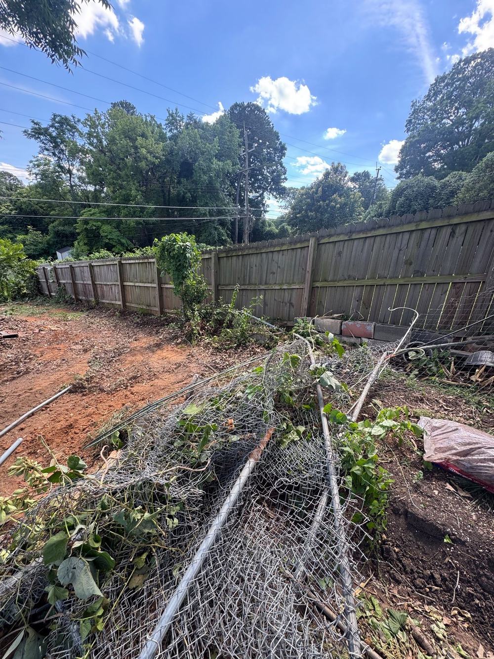 Old chain-link fence and vines pulled and staged before clearing a backyard in Huntersville NC