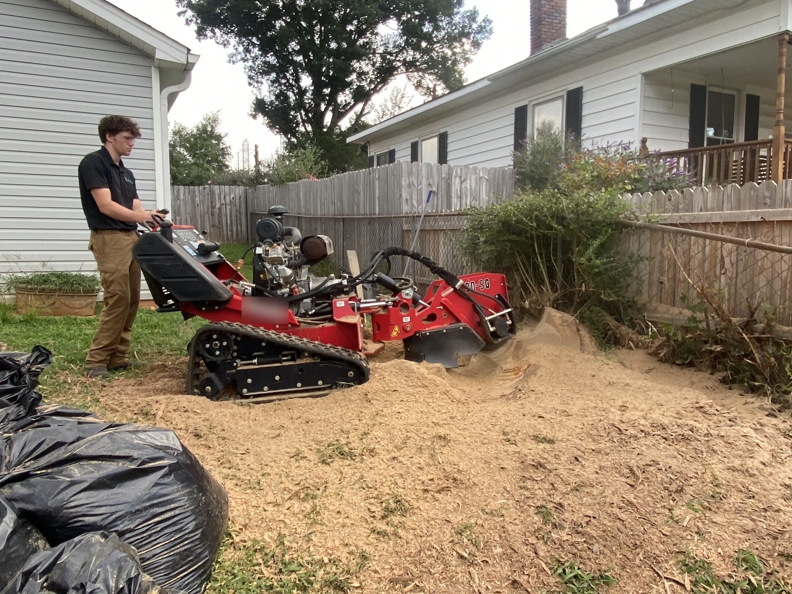Operator running a tracked walk-behind stump grinder in a Charlotte NC backyard